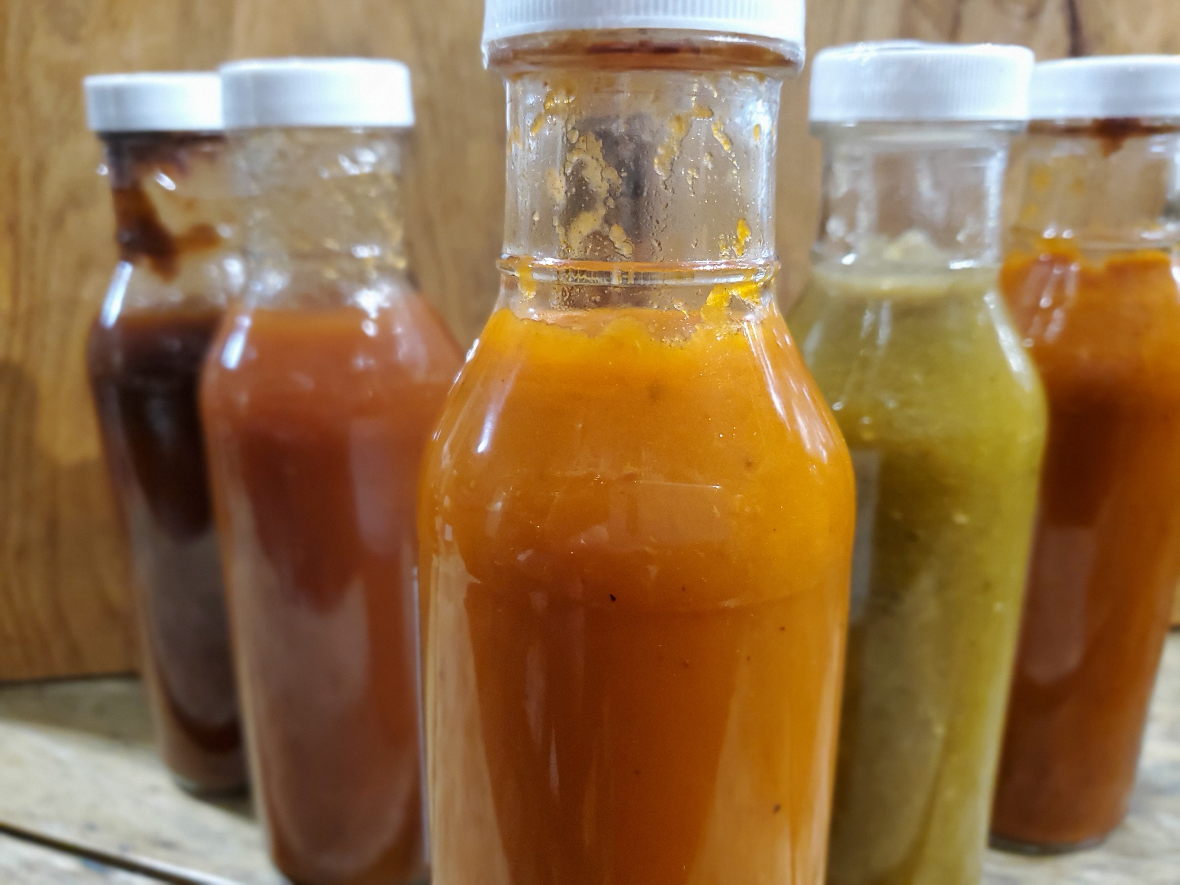 Orange, Green, Brown and Red Sauce In A Collection Of Glass Bottles.